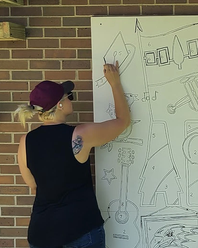 Dayna, in a cap and black tank top, drawing the outline of the Artpark mural on a wall