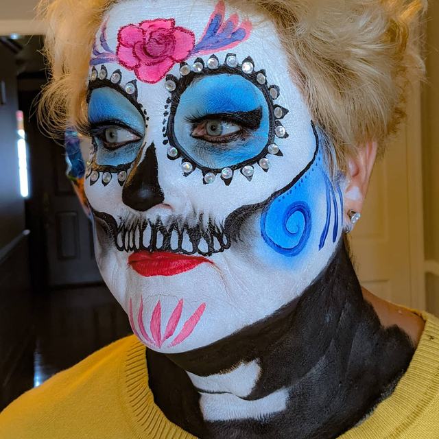 Sugar skull with blue eye sockets, a pink rose and a black painted jaw
