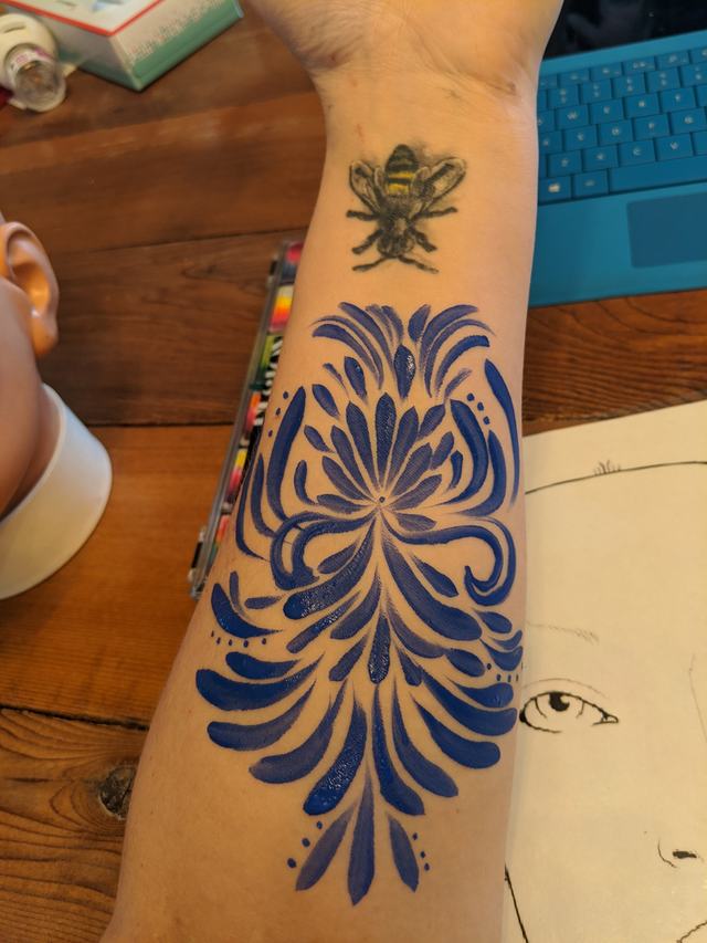 Blue filigree with a bee, painted on a forearm