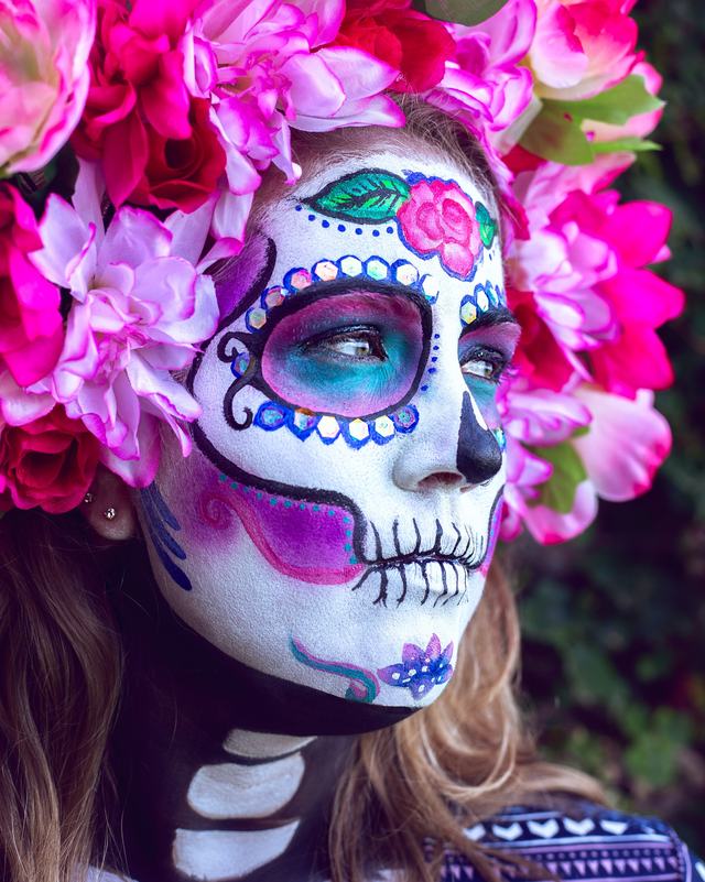 Sugar-skull face and neck painting under a crown of pink and magenta flowers