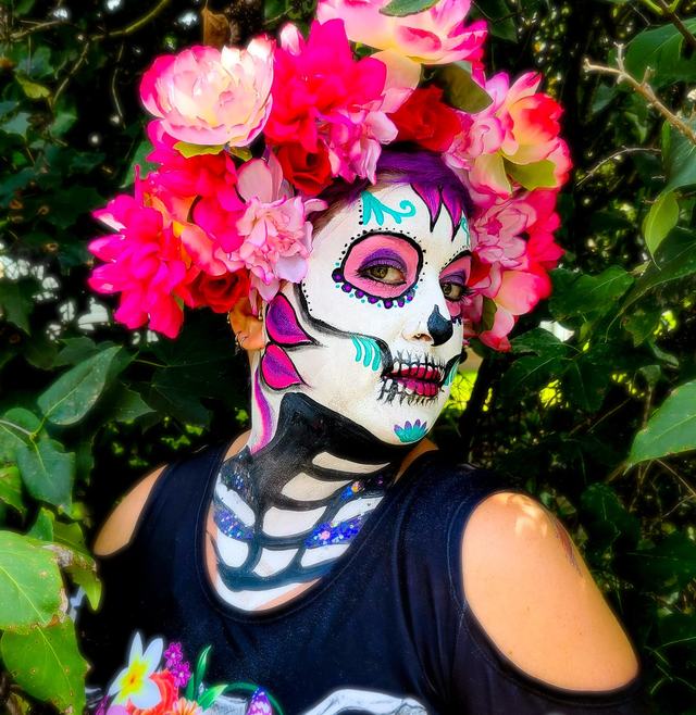 Sugar skull with painted collarbones under a crown of flowers, in a garden