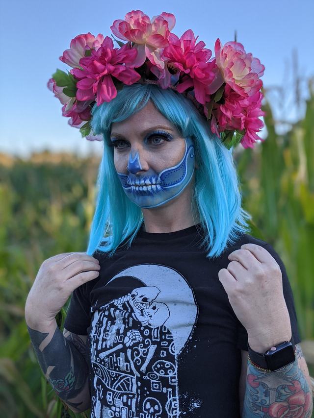 Half-skull face with blue hair and a pink flower crown