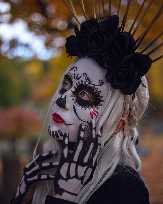 Black-and-white sugar-skull face with a painted skeleton hand and a spiked black-rose halo