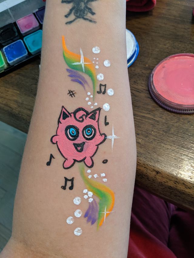 Jigglypuff singing among rainbow swirls on a forearm