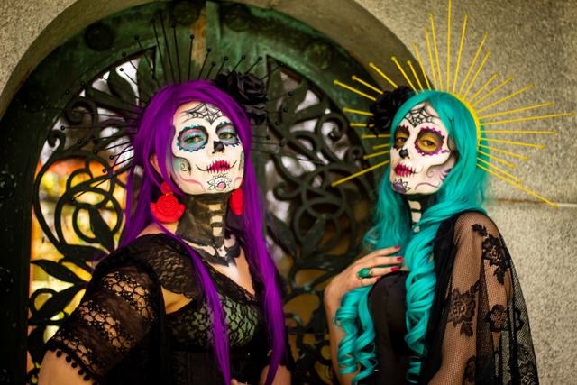 Two sugar-skull looks, one in purple and one in teal with a gold halo, at a wrought-iron gate
